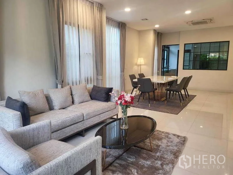 Detached House for rent in Saphan Sung, Bangkok - Bright open-plan living and dining room with grey sofas, sheer drapes and polished tile flooring.