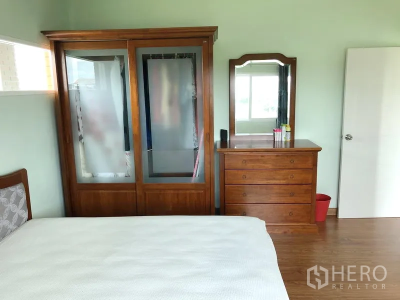 Detached House for rent or sale in Huai Khwang, Bangkok - Bedroom with wooden wardrobe and dresser, light green walls and wood flooring.