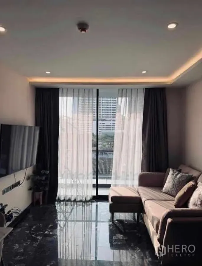 Condominium for rent in Khlong Toei, Bangkok - Sunlit living room with marble floor and sheer curtains opening to balcony.
