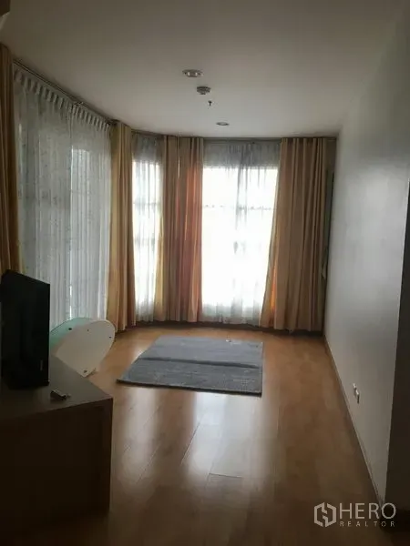 Condominium for rent in Khlong Toei, Bangkok - Corner living room with floor-to-ceiling windows, sheer curtains and drapes, and a small area rug.