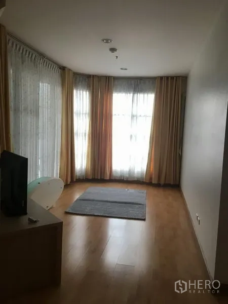 Condominium for rent in Khlong Toei, Bangkok - Corner living room with floor-to-ceiling windows, sheer curtains and drapes, and a small area rug.