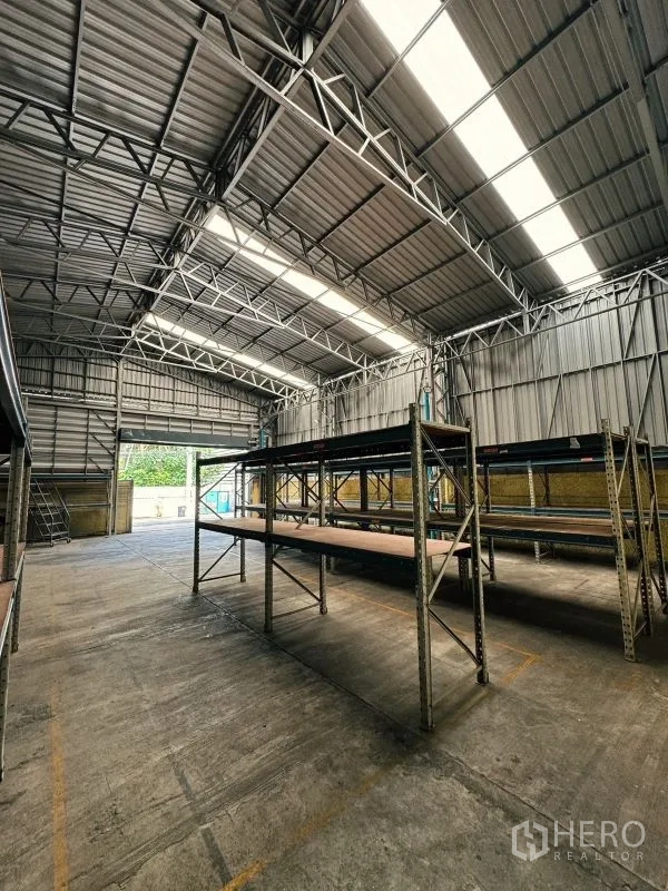 Warehouse for rent in Din Daeng, Bangkok - Interior view showing racking systems and large rolling door with translucent roof panels.