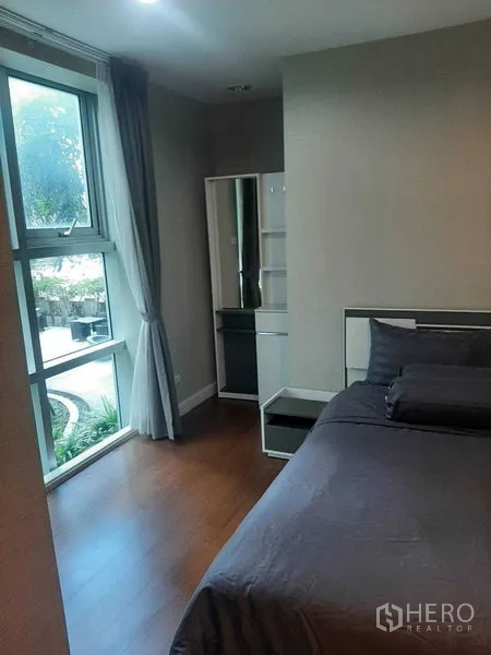 Condominium for rent or sale in Huai Khwang, Bangkok - Bedroom corner with tall window, dressing mirror and courtyard outlook.