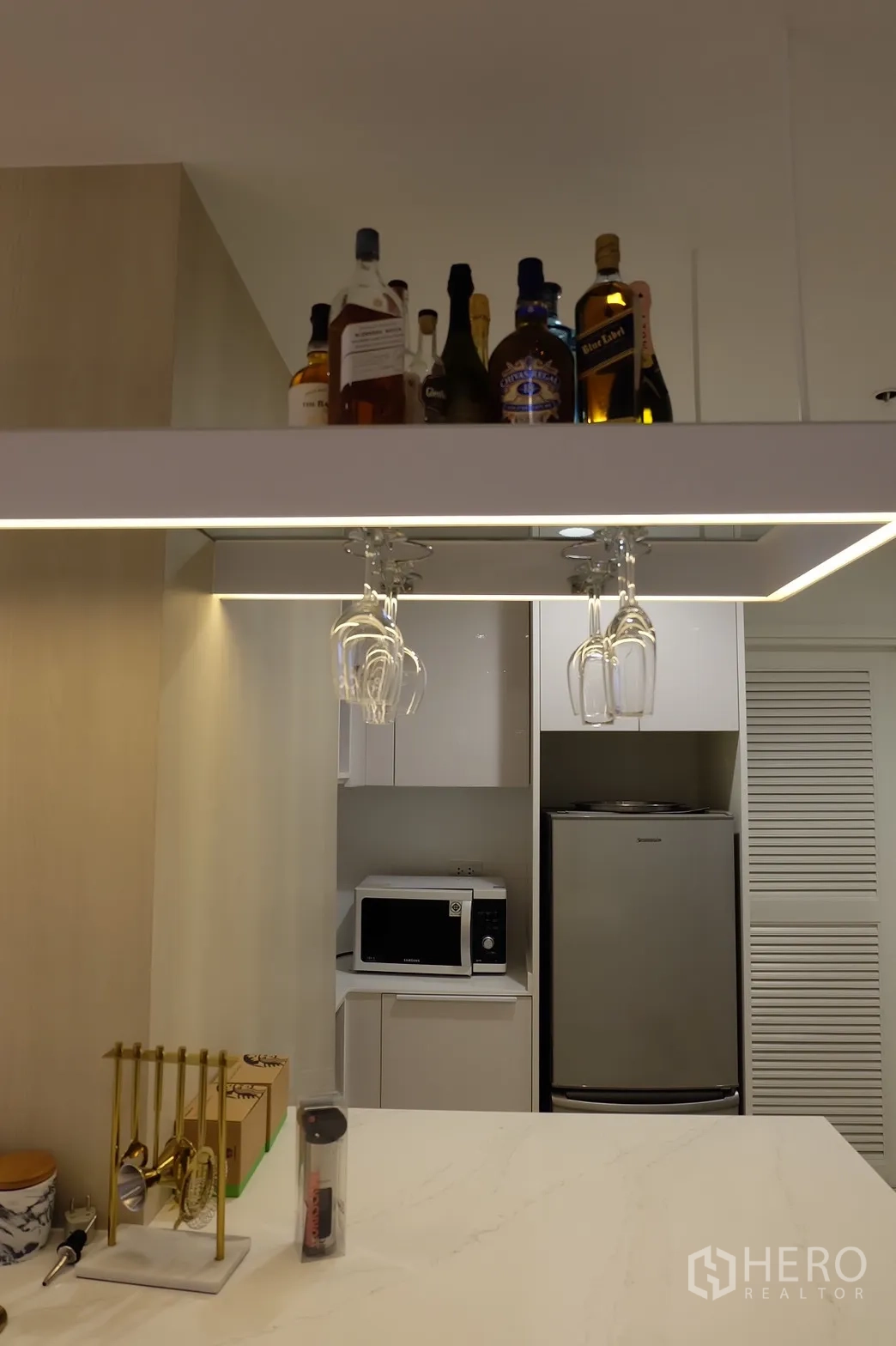 公寓 出租在Bang Rak, Bangkok - 近景：岛台上方的酒架与悬挂酒杯。