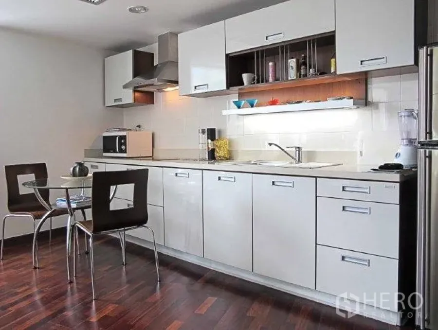Condominium for rent in Pathum Wan, Bangkok - Bright condo kitchen with white cabinetry, under-cabinet lighting, glass dining table and hardwood floors.
