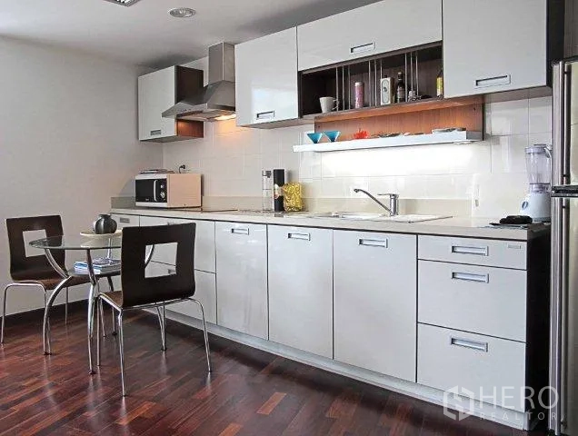 Condominium for rent in Pathum Wan, Bangkok - Bright condo kitchen with white cabinetry, under-cabinet lighting, glass dining table and hardwood floors.
