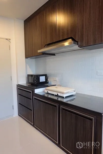 Detached House for rent in Bang Phli, Samut Prakan - Kitchen with dark wood cabinets, stone countertop, hood and white subway tile backsplash.