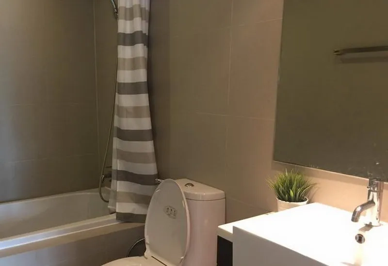 Condominium for rent in Khlong Toei, Bangkok - Modern bathroom with bathtub and shower, striped curtain, toilet, and vanity with mirror.
