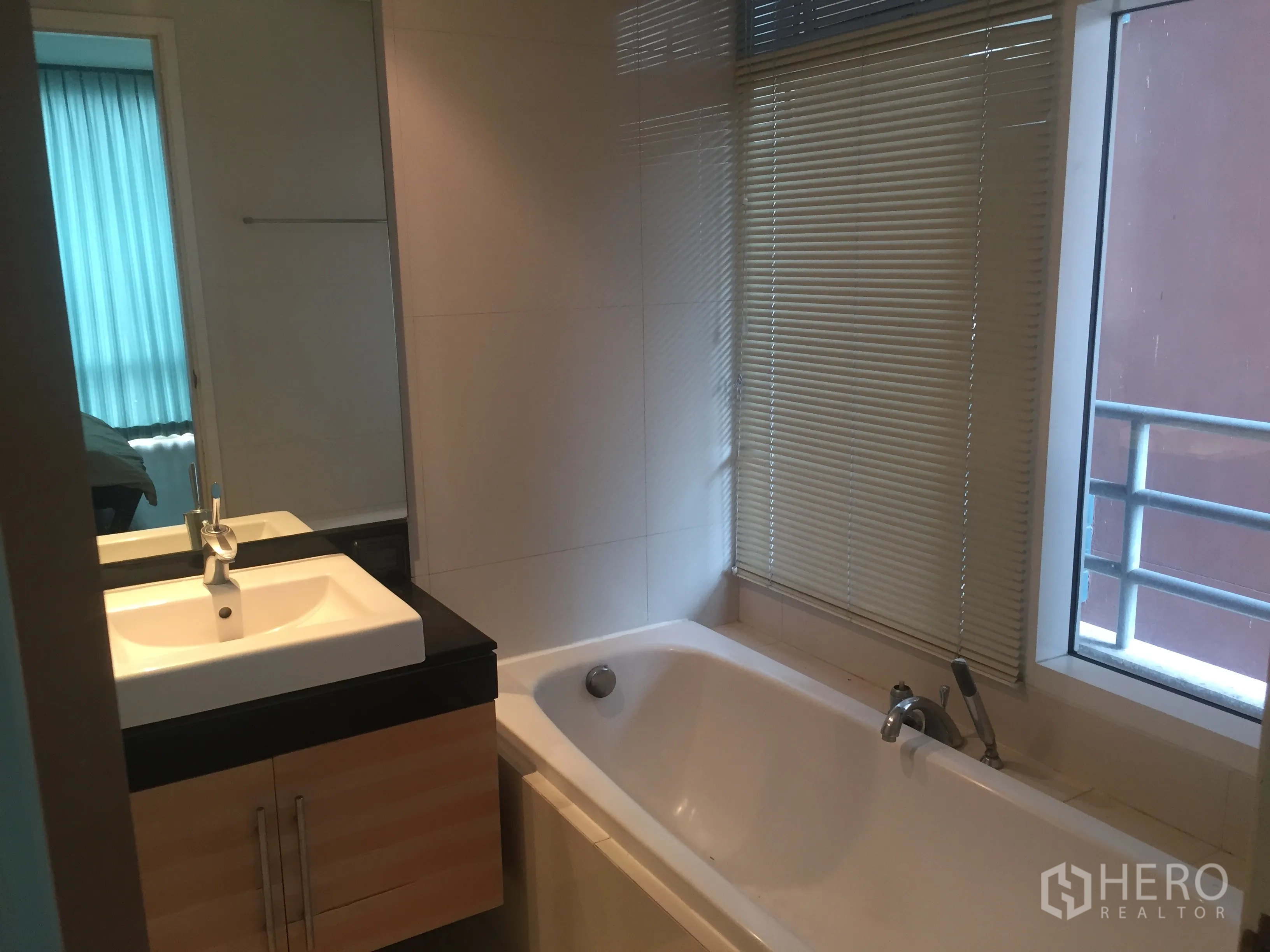 Condominium for rent or sale in Watthana, Bangkok - Bathroom featuring a long soaking bathtub beside a window and a vanity with mirror.
