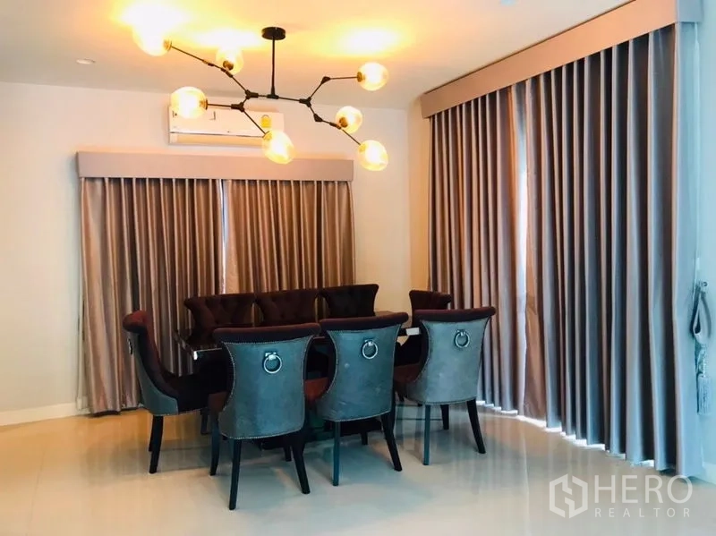 独立式住宅 出租或出售在Pathum Thani - 餐厅八人餐桌，吊灯和整面窗帘