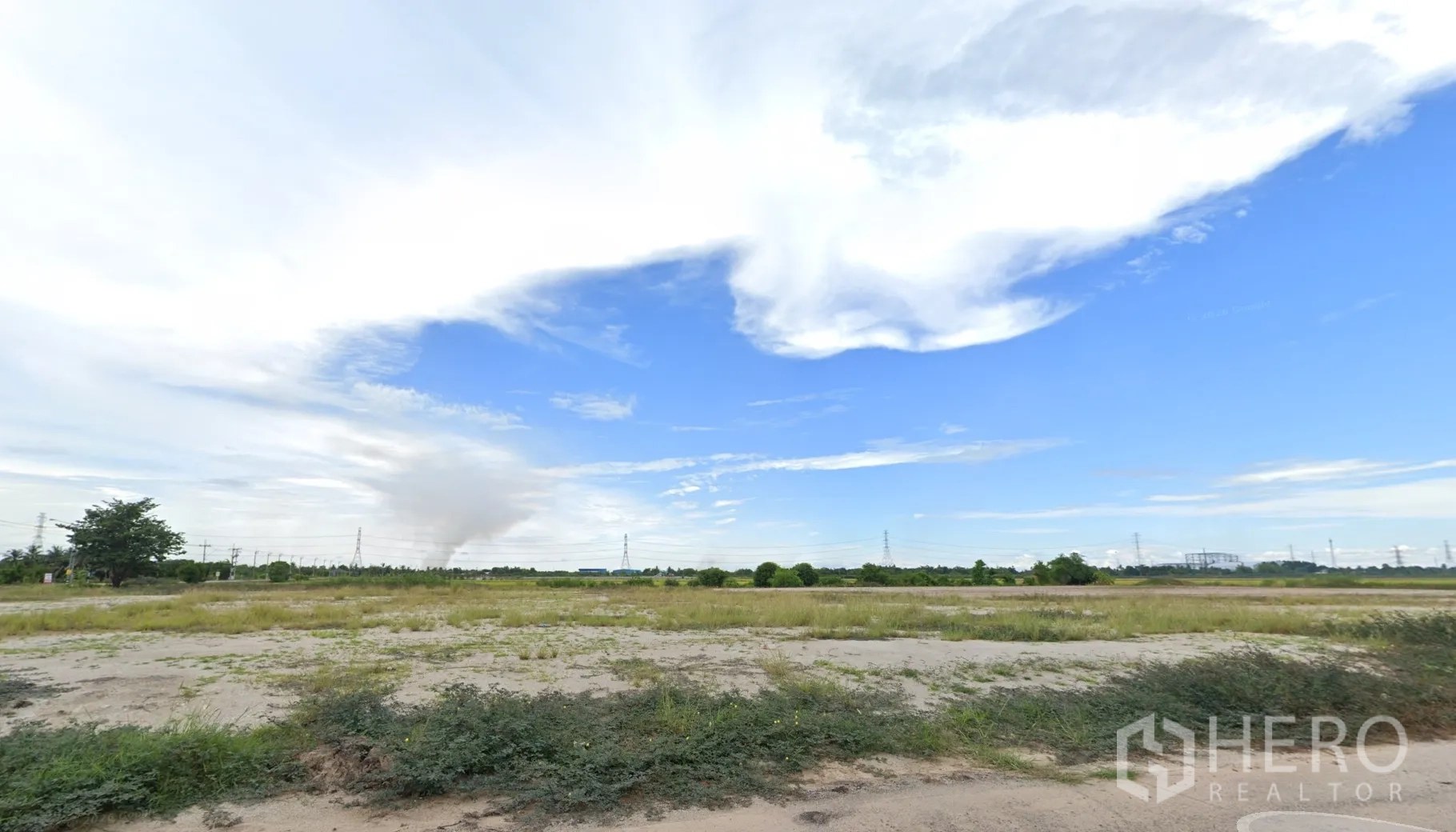 Land for sale in Sai Noi, Nonthaburi - Wide view of level land with light vegetation and transmission towers on the horizon.