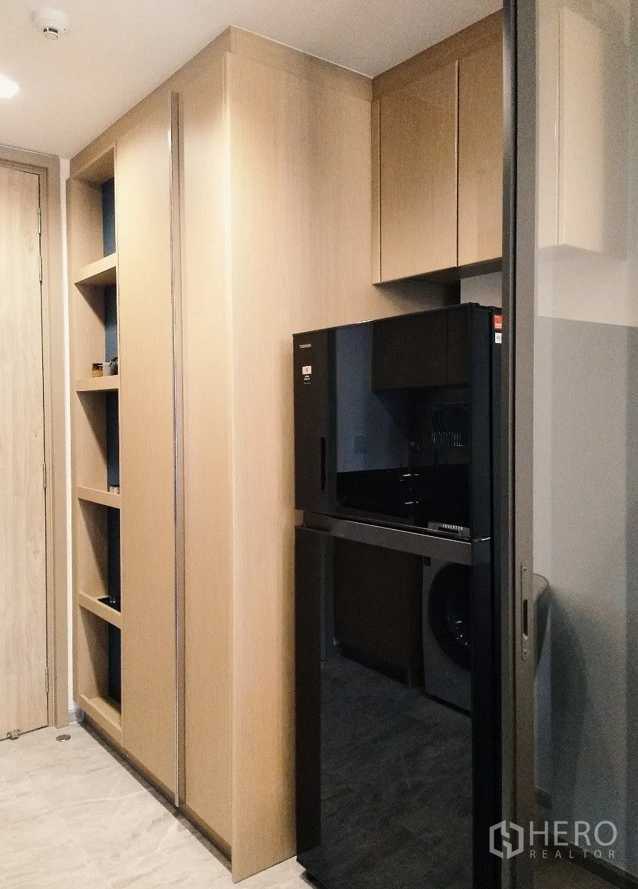 公寓 for rent in Watthana, Bangkok - 厨房一侧设黑色冰箱与内嵌橱柜，旁有玻璃隔断。