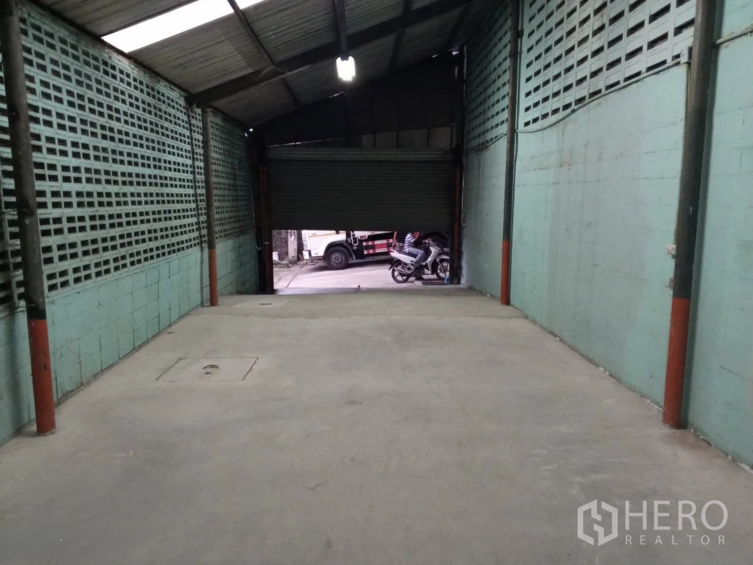 Warehouse for rent in Min Buri, Bangkok - Loading zone facing a partially opened roller door with driveway access for trucks.