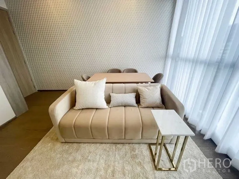 Condominium for rent in Ratchathewi, Bangkok - Bright living and dining area with beige sofa, four-seat table and floor-to-ceiling sheer curtains in a Ratchathewi condo.