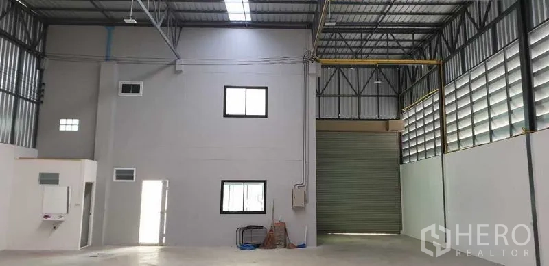 Factory for rent in Lam Luk Ka, Pathum Thani - High-ceiling warehouse interior with steel trusses, internal office block and wide roller shutter door.