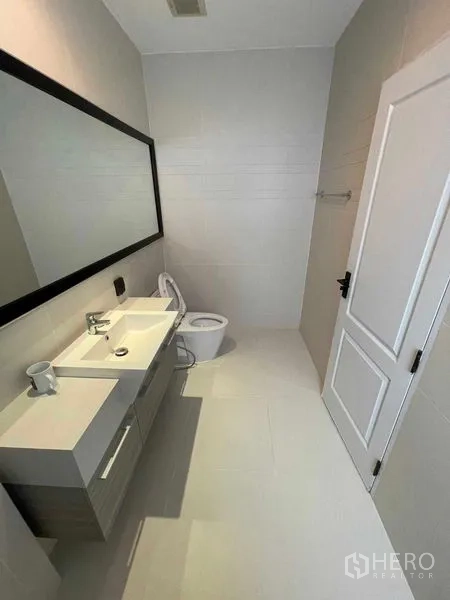 Detached House for sale in Mueang Samut Prakan, Samut Prakan - Minimalist bathroom with long vanity, full-height mirror and white tiling.