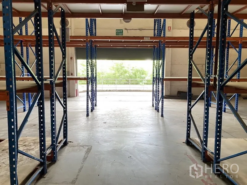 คลังสินค้า ให้เช่าในBang Phli, Samut Prakan - ทางเดินในโกดังมองไปยังประตูม้วน พร้อมชั้นวางและพื้นคอนกรีตเรียบ