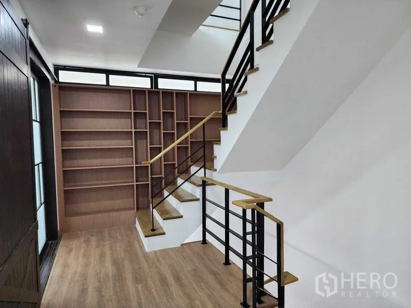 带办公室的家 出租在Prawet, Bangkok - 楼梯间采用黑色金属扶手，墙面为通高木质书柜，储物充足。