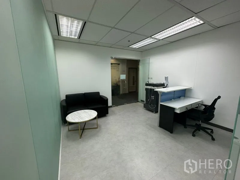 Office Space for rent - Reception and workstation area with black sofa, round marble coffee table and glass partition walls.