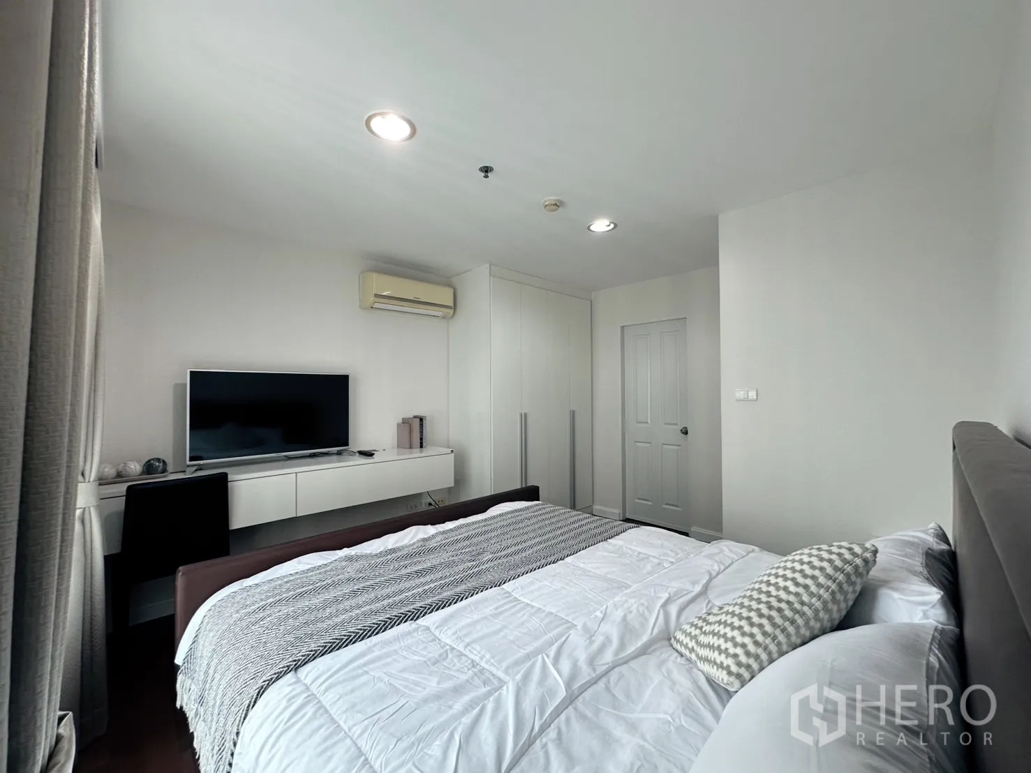 คอนโด for sale in Huai Khwang, Bangkok - ห้องนอนหลักสว่างพร้อมเตียงคิง ทีวี บิ้วท์อินตู้เสื้อผ้า โต๊ะทำงาน และเครื่องปรับอากาศ.