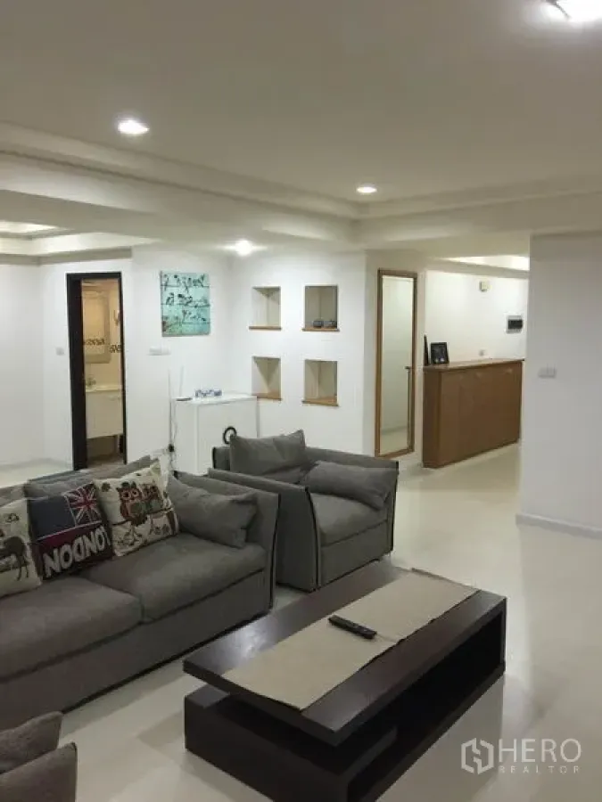 Condominium for rent or sale in Watthana, Bangkok - Spacious living room with grey sofas, recessed ceiling lights and wall niches in a modern Sukhumvit condominium.