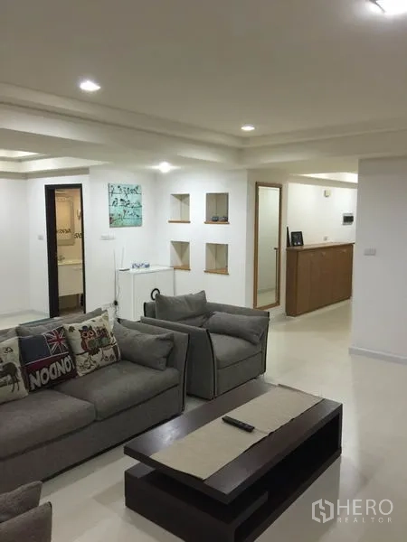 Condominium for rent or sale in Watthana, Bangkok - Spacious living room with grey sofas, recessed ceiling lights and wall niches in a modern Sukhumvit condominium.
