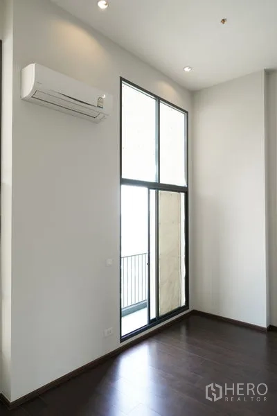Condominium for sale in Watthana, Bangkok - Bright living space with floor-to-ceiling window and balcony door over dark wood floors.