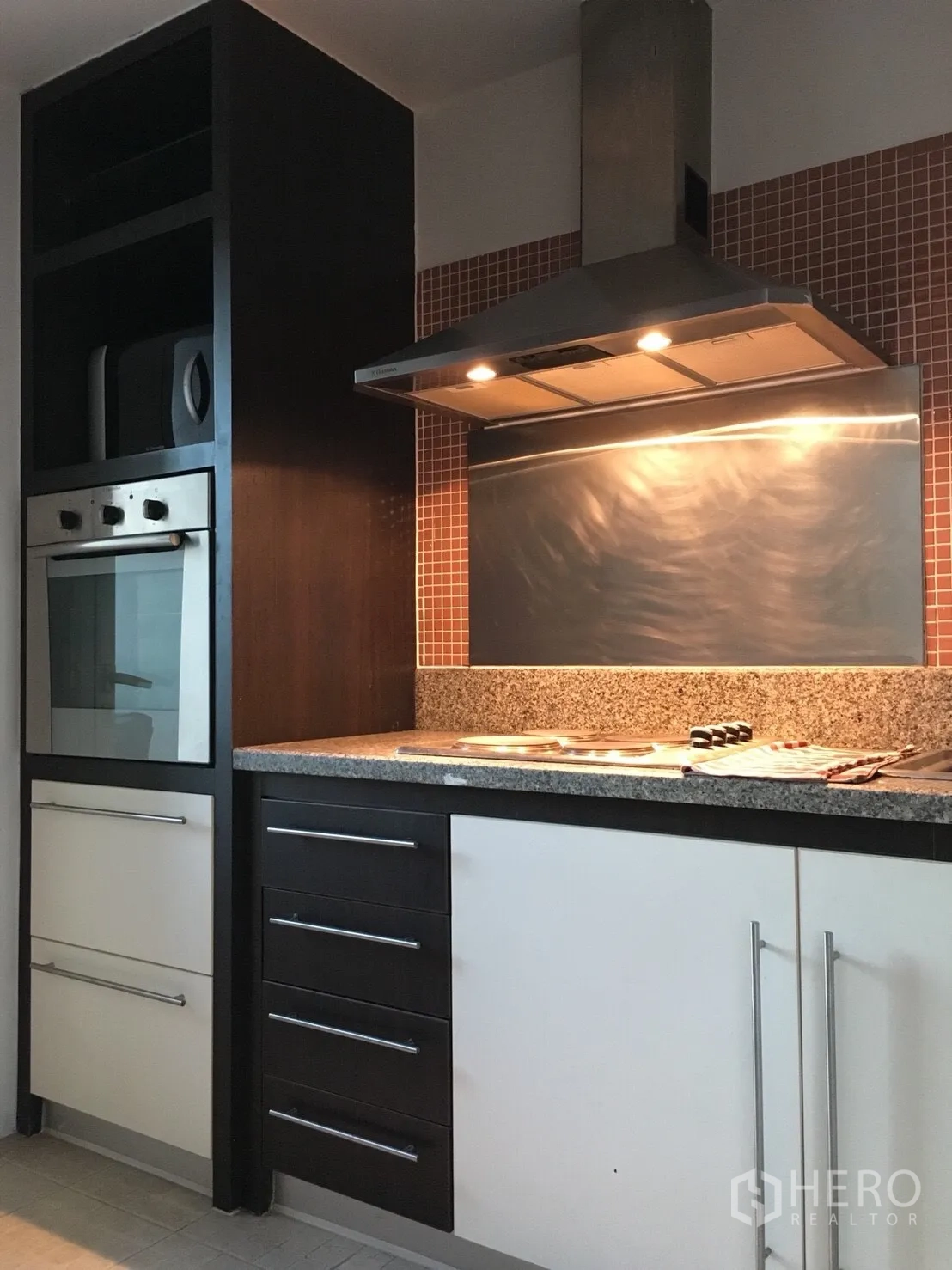 Condominium for rent in Watthana, Bangkok - Modern kitchen with granite countertop, built-in oven, cooktop, and a stainless-steel range hood.
