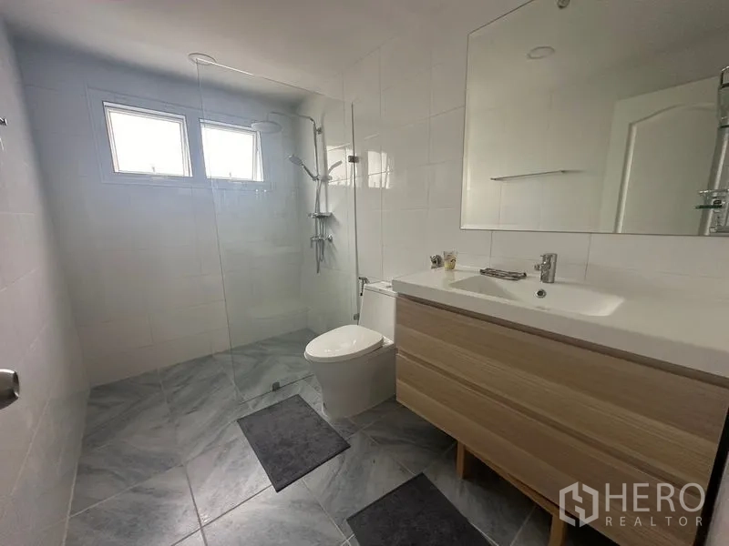 Condominium for rent - Bright bathroom with walk-in glass shower, vanity and toilet beneath twin windows.