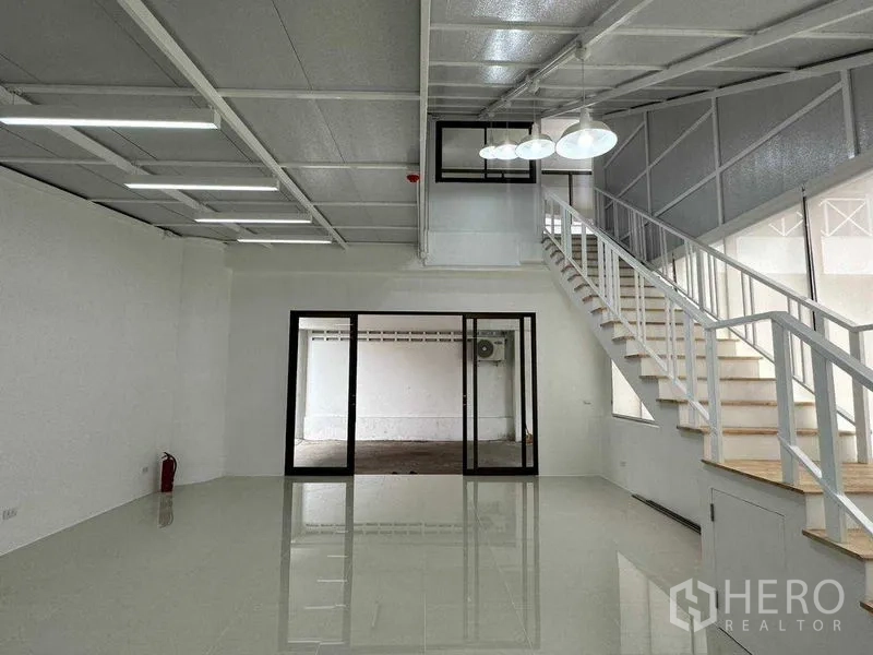 Office Space for rent or sale in Khlong Toei, Bangkok - Main hall featuring a mezzanine staircase and glass sliding doors to a separate room.