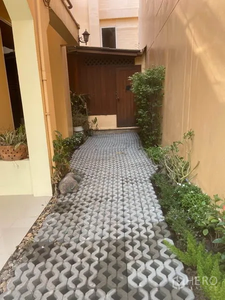 Detached House for rent in Watthana, Bangkok - Paved side walkway with greenery leading to a wooden door.