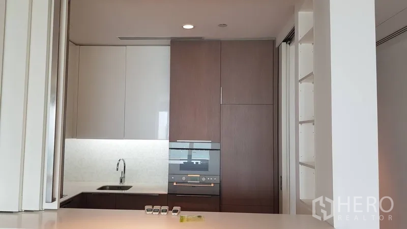 Condominium for rent in Pathum Wan, Bangkok - Modern kitchenette with built-in oven, tall cabinets and stone countertops.