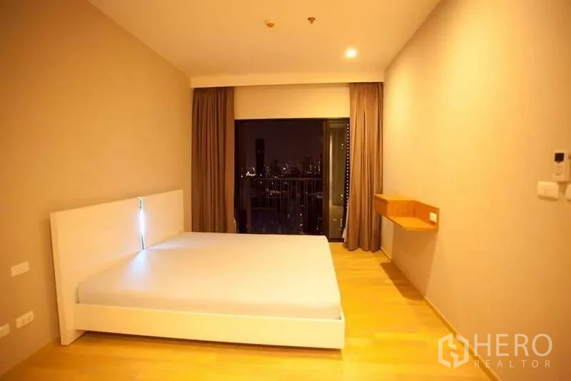 Condominium for rent or sale in Watthana, Bangkok - Bedroom with city night view from large window and a small wall-mounted desk.