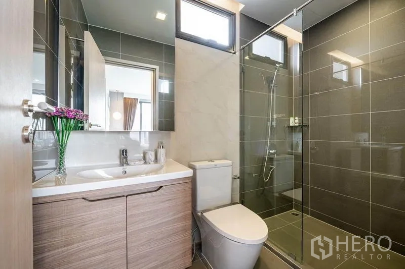 公寓 出租或出售在Watthana, Bangkok - 第二浴室，玻璃淋浴间、洗手台、采光窗与灰色墙砖。