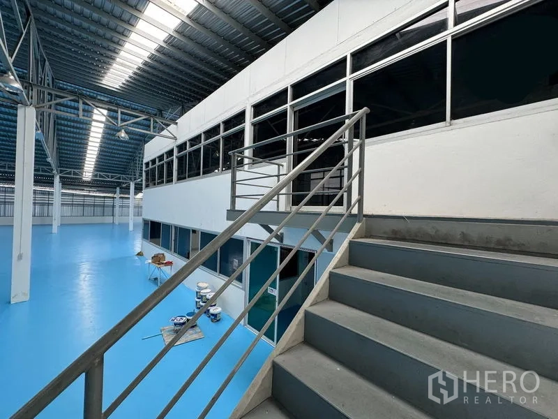 货栈 出租在Mueang Pathum Thani, Pathum Thani - 通往夹层办公室的楼梯，俯瞰仓库地面与天窗屋顶。