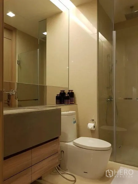 Condominium for rent in Watthana, Bangkok - Compact bathroom with glass shower enclosure, large mirror and light wood vanity.