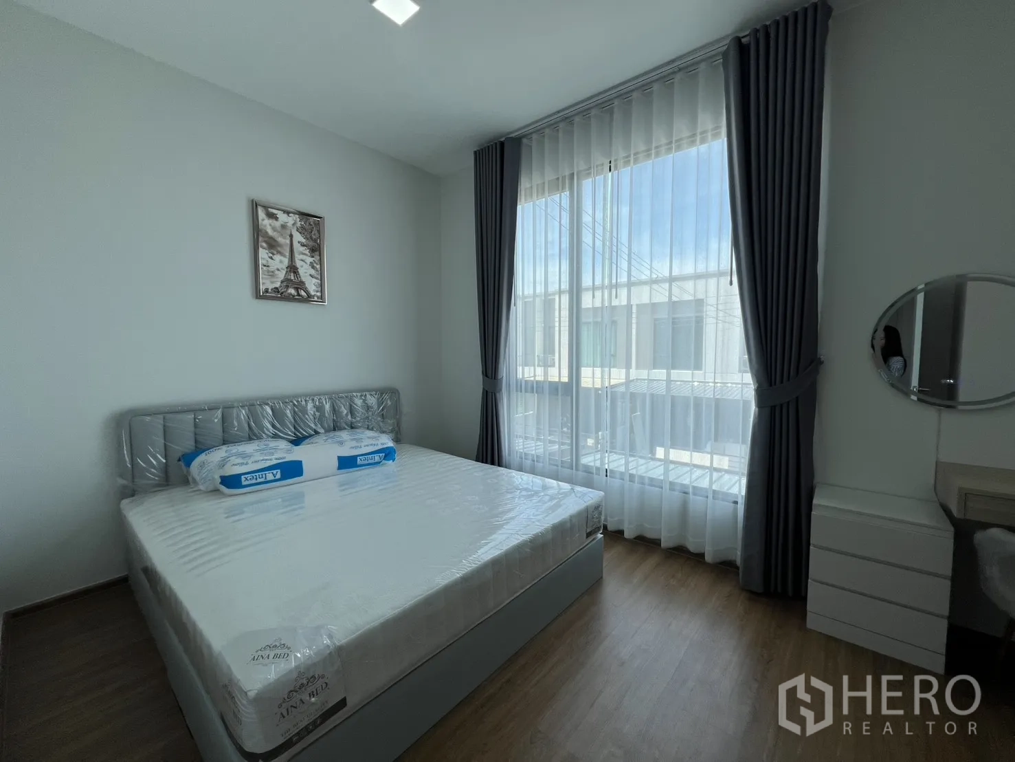 Townhouse for rent in Bang Phli, Samut Prakan - Master bedroom corner with bed, vanity and round mirror by the window.