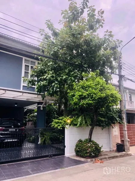 Detached House for rent in Bang Kapi, Bangkok - Side view of the house with tall trees, boundary wall and a quiet residential street.