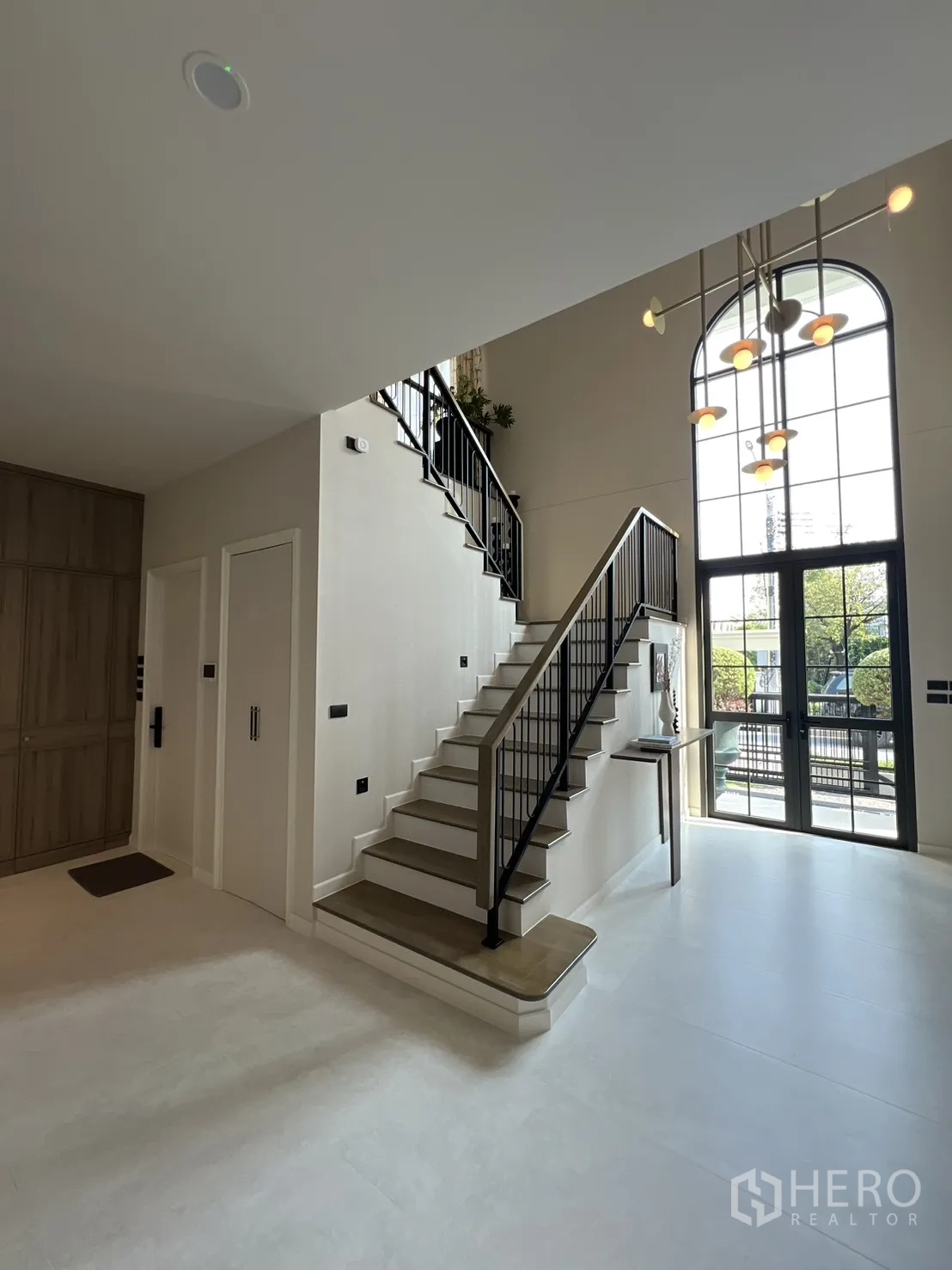 บ้านเดี่ยว for rent in Bang Phli, Samut Prakan - โถงทางเข้าเพดานสูงพร้อมบันได ราวเหล็กสีดำ และหน้าต่างโค้งกับโคมไฟแขวน