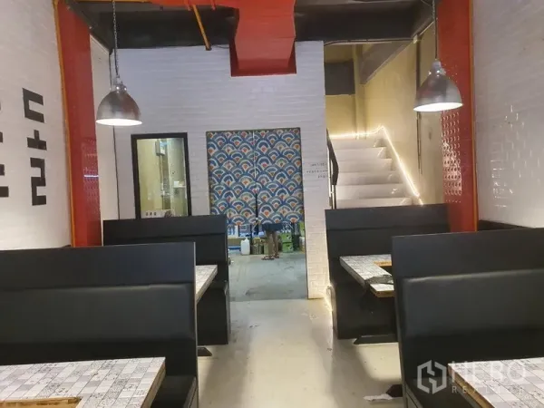 อาคารพาณิชย์ ให้เช่าในKhlong Toei, Bangkok - โซนรับประทานอาหารชั้นล่าง บูธนั่งสีดำ มองไปยังพื้นที่เตรียมครัวและบันได ผนังกระเบื้องสีขาว