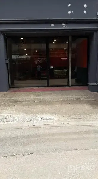 Shophouse for rent in Bang Khen, Bangkok - Street-level facade with a wide glass entrance and dark exterior, with roadway in front.