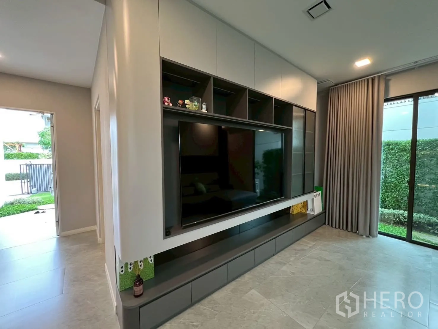 Detached House for rent in Samut Prakan - Built-in TV wall and media storage with garden views from wide glass doors.