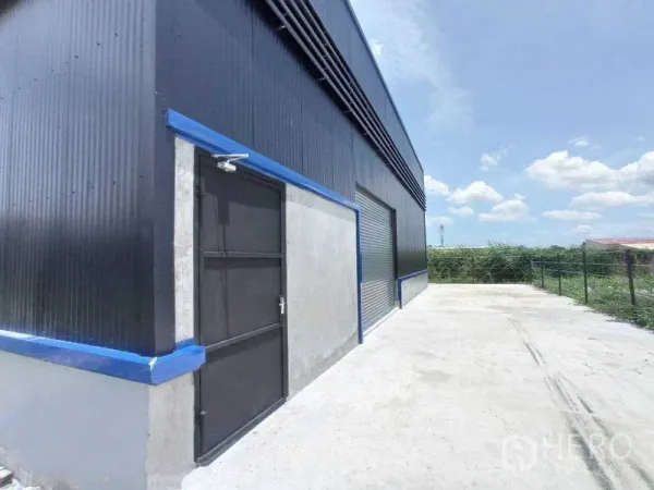 คลังสินค้า ให้เช่าในSaphan Sung, Bangkok - ด้านนอกโกดังผนังเมทัลชีทสีดำ ประตูคนเดิน ประตูม้วน และลานคอนกรีตกว้าง