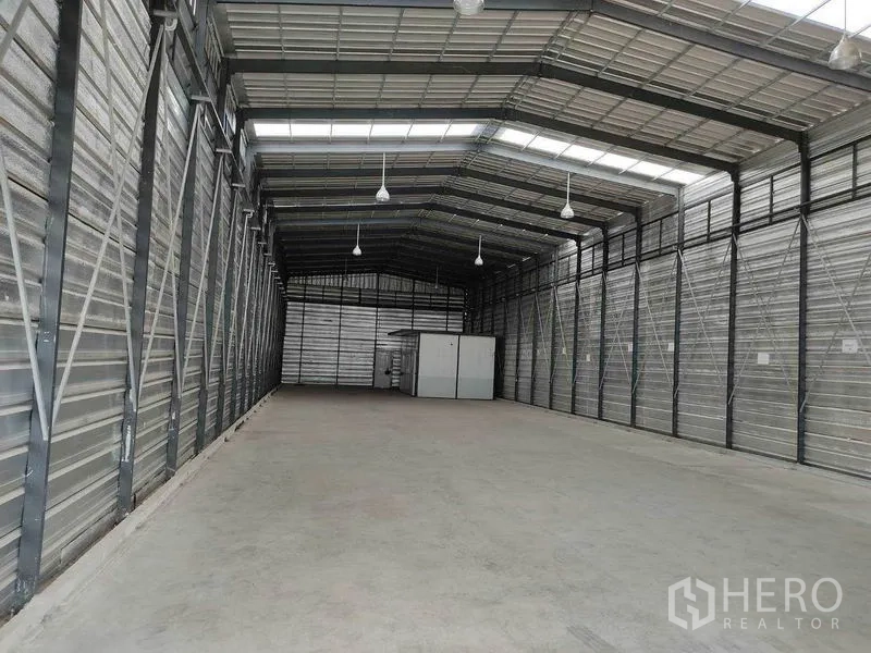 Warehouse for rent in Bang Phli, Samut Prakan - Deep storage space with metal walls, pendant lights and an internal office at the far end.