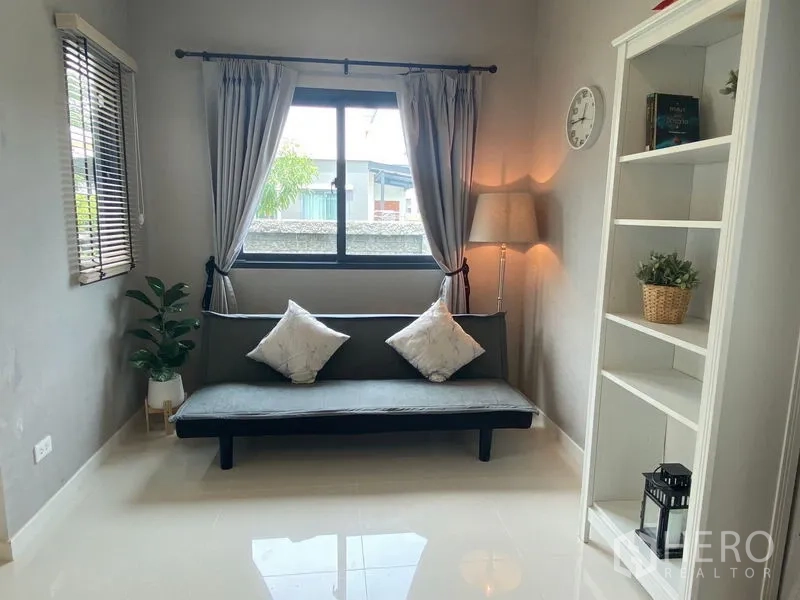 Detached House for rent in Bang Phli, Samut Prakan - Cozy reading nook with a sofa, window drapes, floor lamp and open shelving.