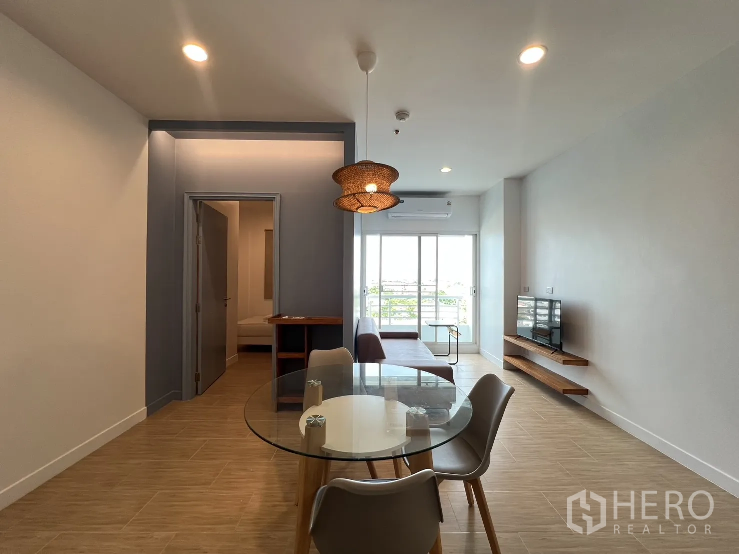 Condominium for rent in Bang Kapi, Bangkok - Open living and dining area with round glass table, sofa, TV, and sliding doors to a balcony.