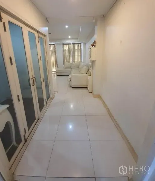 Townhouse for rent in Phaya Thai, Bangkok - Long hallway with white tiled flooring, frosted glass doors and a view toward the sunlit lounge.