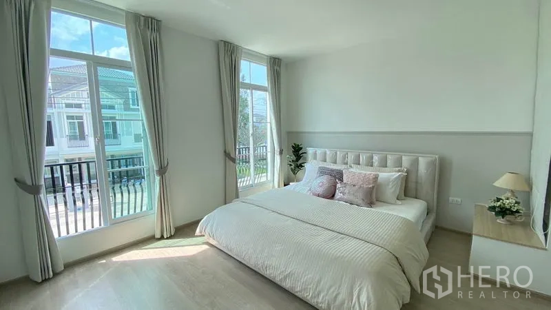 联排别墅 出租在Prawet, Bangkok - 主卧充足采光，大窗与法式阳台栏杆，浅色系