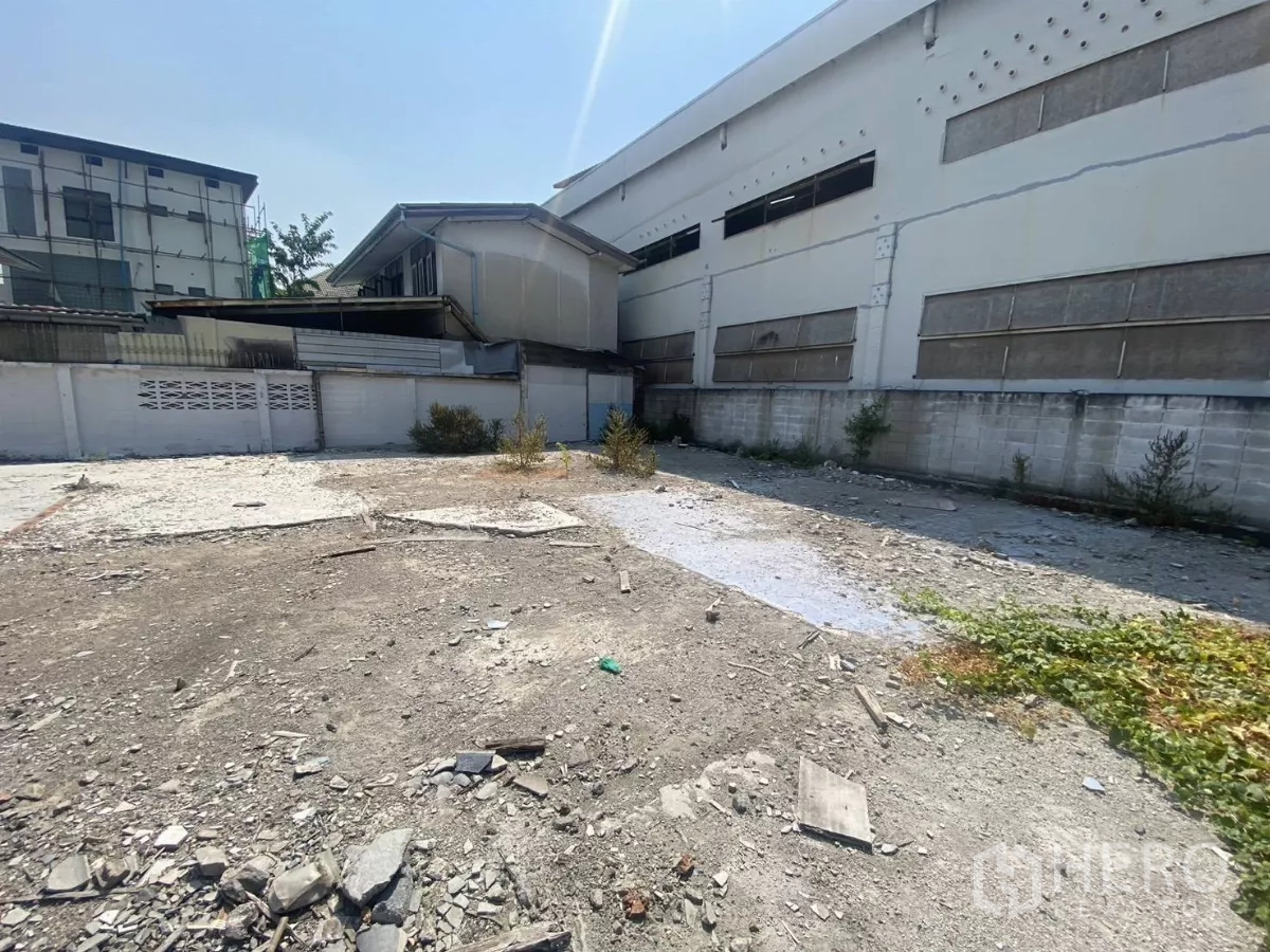 Land for rent in Khlong Toei, Bangkok - Vacant urban lot beside a large industrial-style building and boundary wall, level ground.