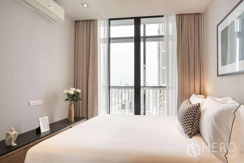 Condominium for rent in Khlong Toei, Bangkok - Bedroom with large bed and full-height windows offering a city view and balcony access.